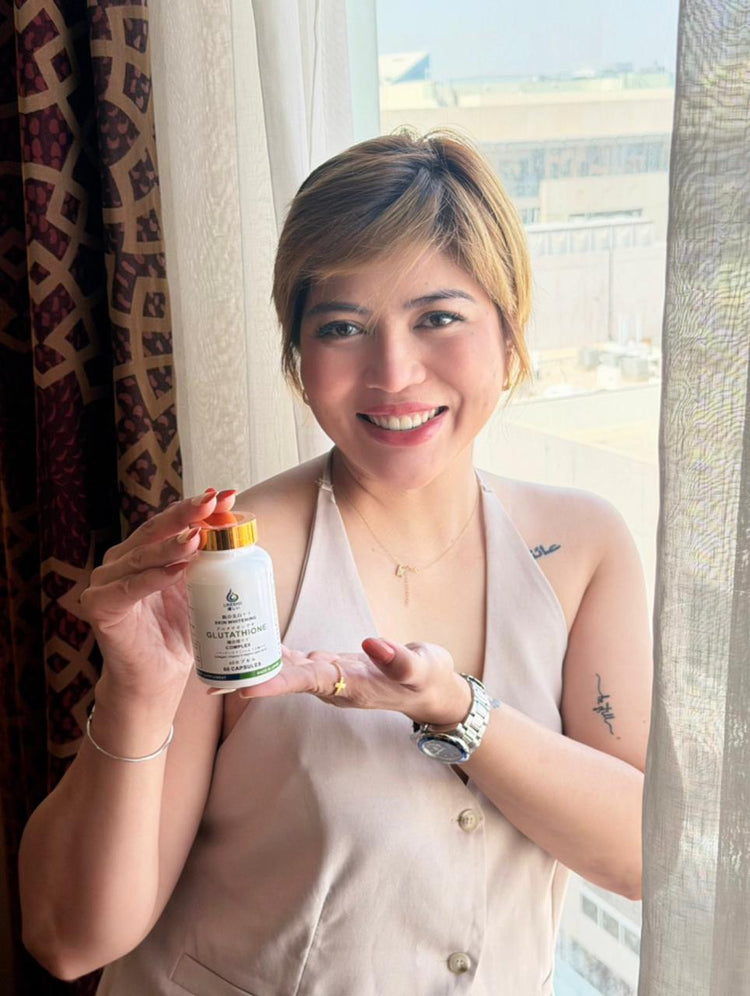 Smiling woman presenting a bottle of Ureshii Glutathione Complex in a bright window-lit setting, highlighting a daily wellness supplement for beauty and skin support.